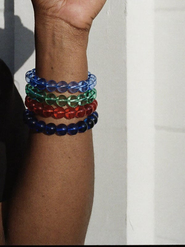 A wrist wears four bracelets of blue, green and red recycled glass beads