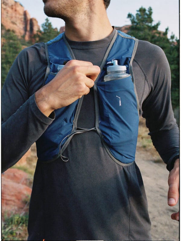 A runner tightens the chest strap of a blue trail running vest on a mountain trail